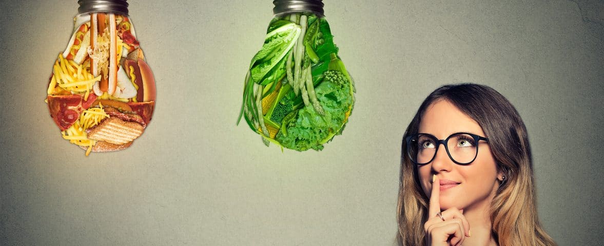 Portrait beautiful woman in glasses thinking looking up at junk food and green vegetables shaped as light bulb isolated on gray background. Diet choice right nutrition healthy lifestyle concept
